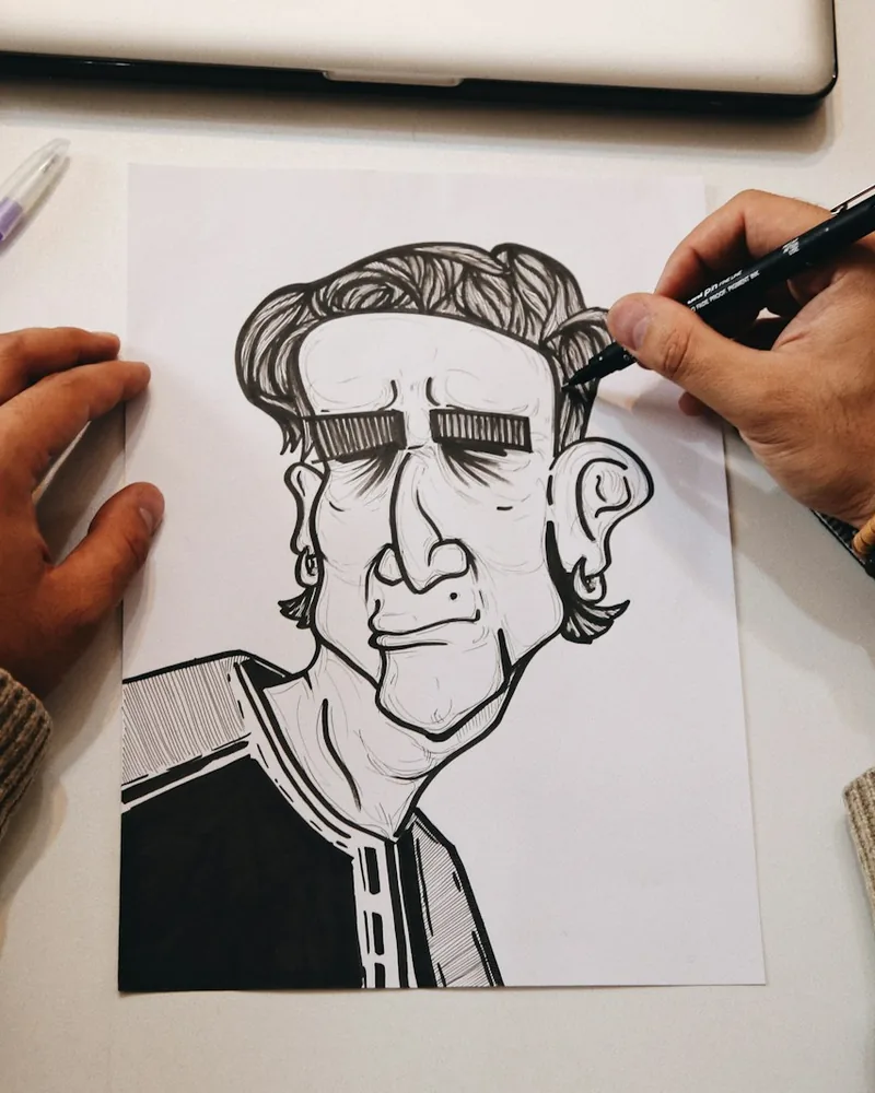 Mano trazando líneas con pluma sobre papel blanco, detalle del trabajo de entintado